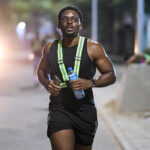 Nigerian musician Jarell Ebuka running outdoors at night while wearing a reflective harness and holding a water bottle, demonstrating his commitment to fitness and endurance.