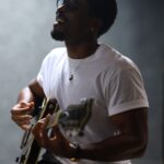 Nigerian artist Jarell Ebuka smiling while playing an electric guitar in a studio, simulating an intimate acoustic set.