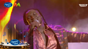 Francis Atela delivering a soulful live singing performance on Nigerian Idol Season 6 while wearing a metallic patterned jacket under warm stage lights.