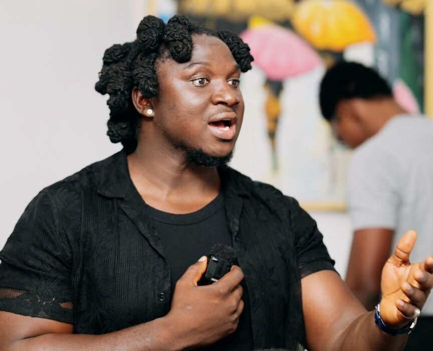 Nigerian folk singer-songwriter Francis Atela speaking passionately while holding a lapel microphone during an interactive event.